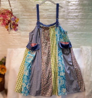 Handmade patchwork apron dress with colorful fabric strips and decorative pockets hanging on display