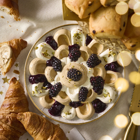 Plate of creamy dessert with blackberries, surrounded by croissants and pastries on a table