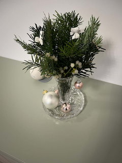 Small decorative Christmas tree with white ornaments on mirrored base against green and white wall