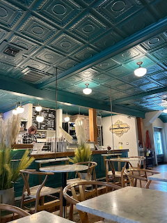 Interior of a coffee shop with tin ceiling, wooden tables, green booth seating, and pendant lights