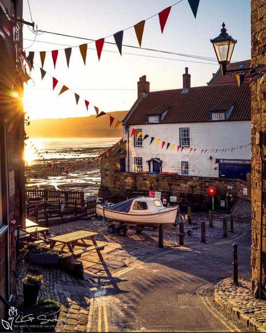 Coblestone slipway in Robin Hood's Bay at sunset with boat, white cottages, bunting, and street lamp