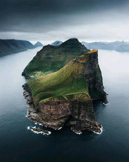 Steep grassy island cliffs rising from the sea under a cloudy sky