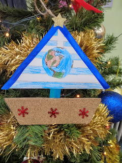 Blue triangle Christmas ornament with gold tinsel on decorated tree