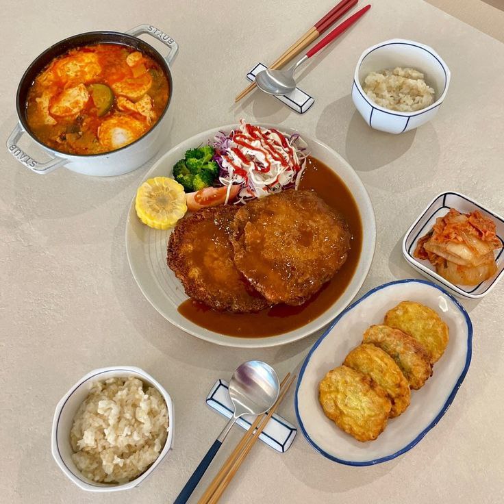 Overhead view of a Korean meal with soup, rice, kimchi, egg rolls, and a sauced cutlet