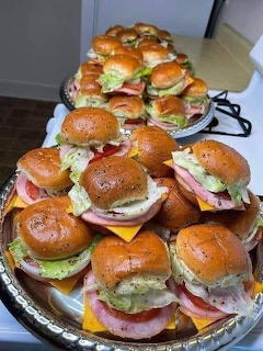 Platter of mini club sandwich sliders with ham, cheese, lettuce and tomato on sesame buns