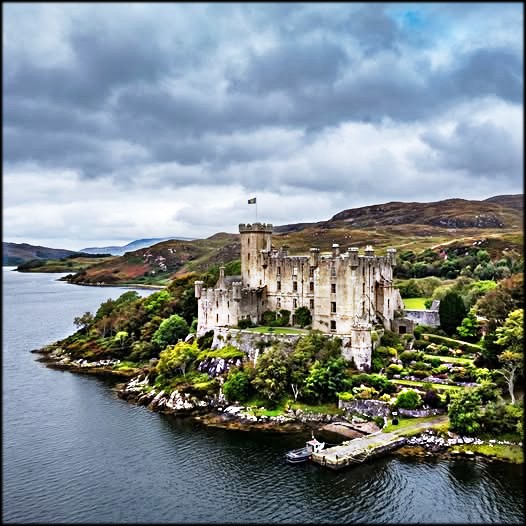 Dunvegan Castle on a rocky shoreline beside calm water under cloudy skies