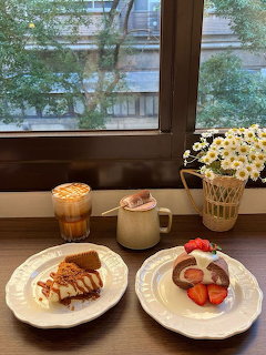 Coffee drinks and desserts on white plates by a window with a vase of daisies