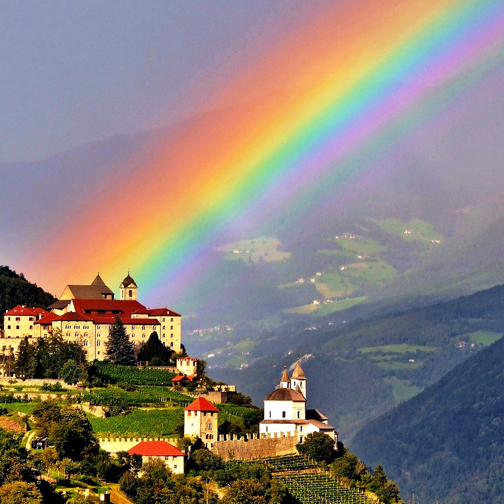 Historic castle and village on hillside with bright rainbow over misty mountain valley