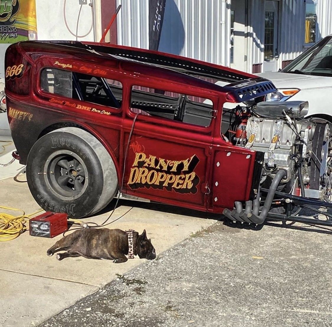 Red custom hot rod with exposed chrome engine and wide rear tires on urban street