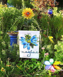 White garden flag with blue flower painting among colorful garden flowers and decorations