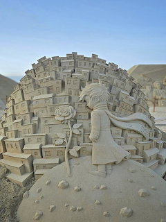 Detailed sand sculpture of a girl figure surrounded by miniature buildings forming a dome shape