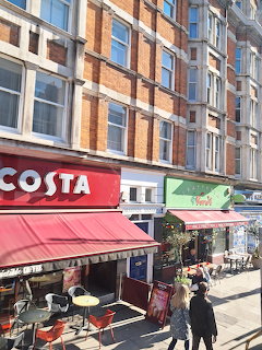 London high street with Costa Coffee shop, red brick building, red awnings, and pedestrians walking on pavement