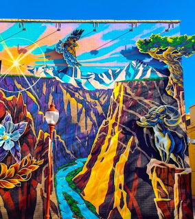 Colorful mural showing desert canyon with ram, eagle, and geometric landscape elements in vivid blues, oranges, and purples