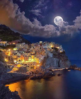 Manarola clifftop village lit at night with full moon and clouds above calm sea