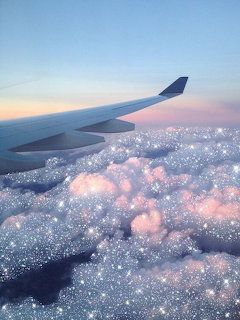 Airplane wing above pink-blue clouds with a sparkling glitter effect