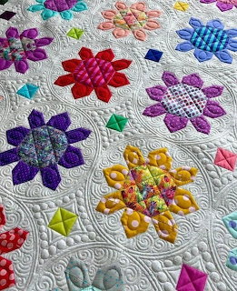 Close-up of a colorful patchwork quilt with flower-shaped blocks and detailed quilting stitches