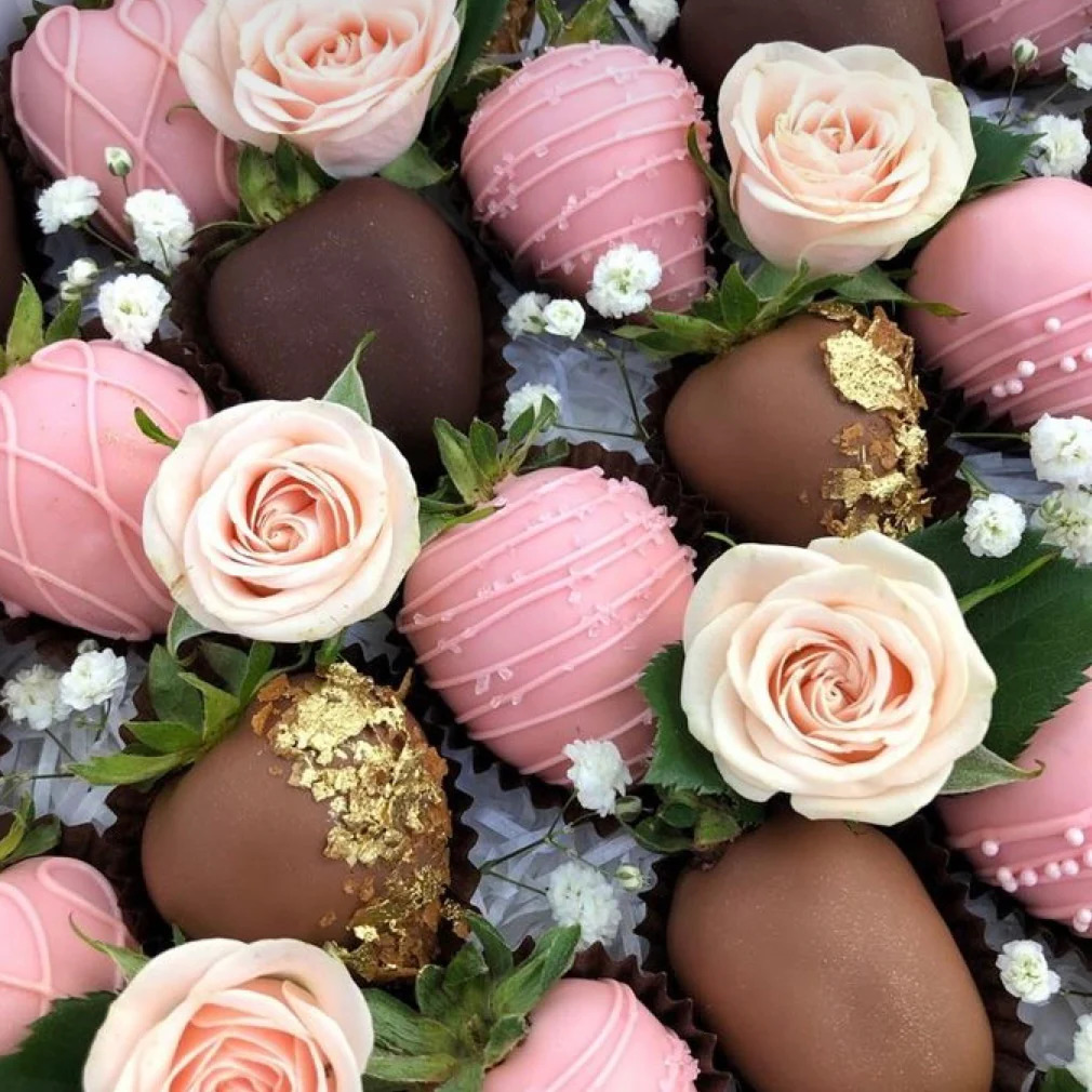 Chocolate-dipped strawberries with pink roses and white flowers arranged on greenery