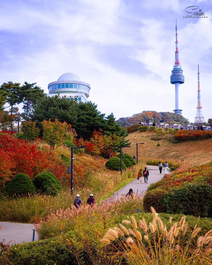 Namsan Park in Seoul during autumn with colorful foliage, walking paths, and N Seoul Tower in the background