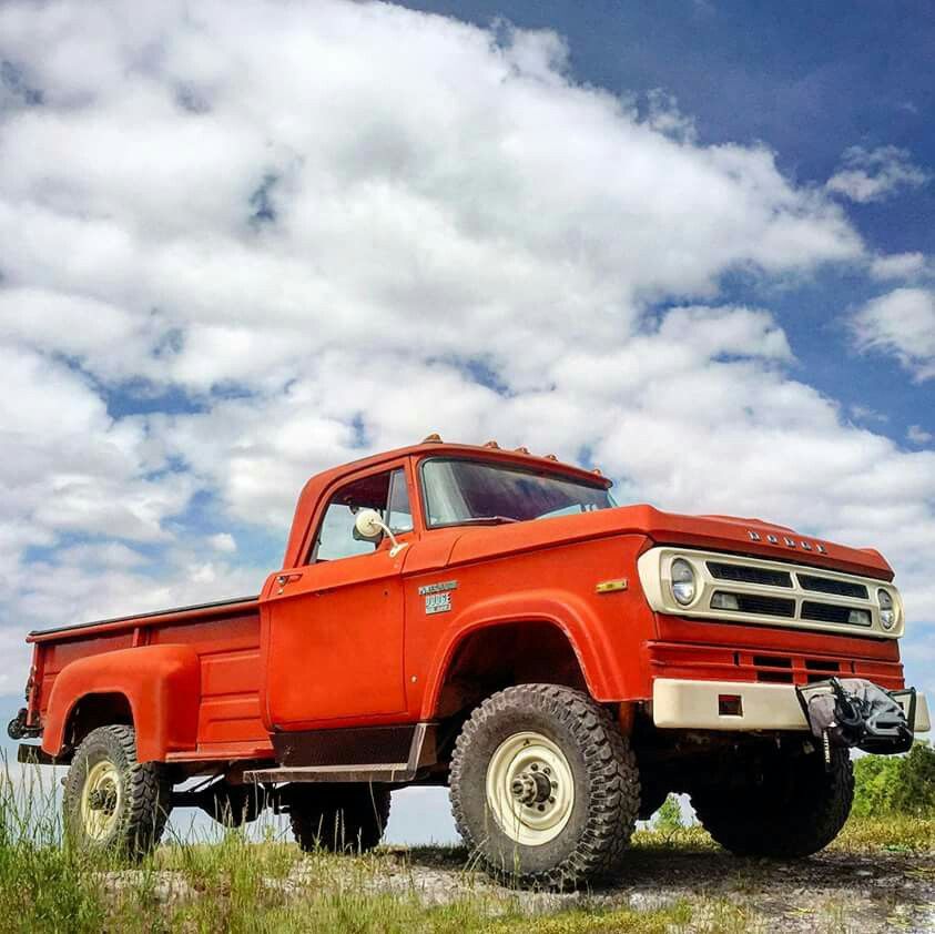 Red vintage pickup truck parked on grass beneath a cloudy blue sky