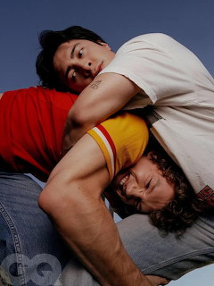 Two young men playfully wrestling outdoors, one in red shirt holding the other in a headlock