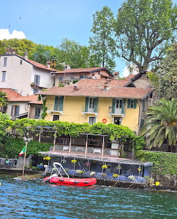 Colorful Italian lakeside houses with green shuters, waterfront terrace, red kayak, and trees along Lake Maggiore