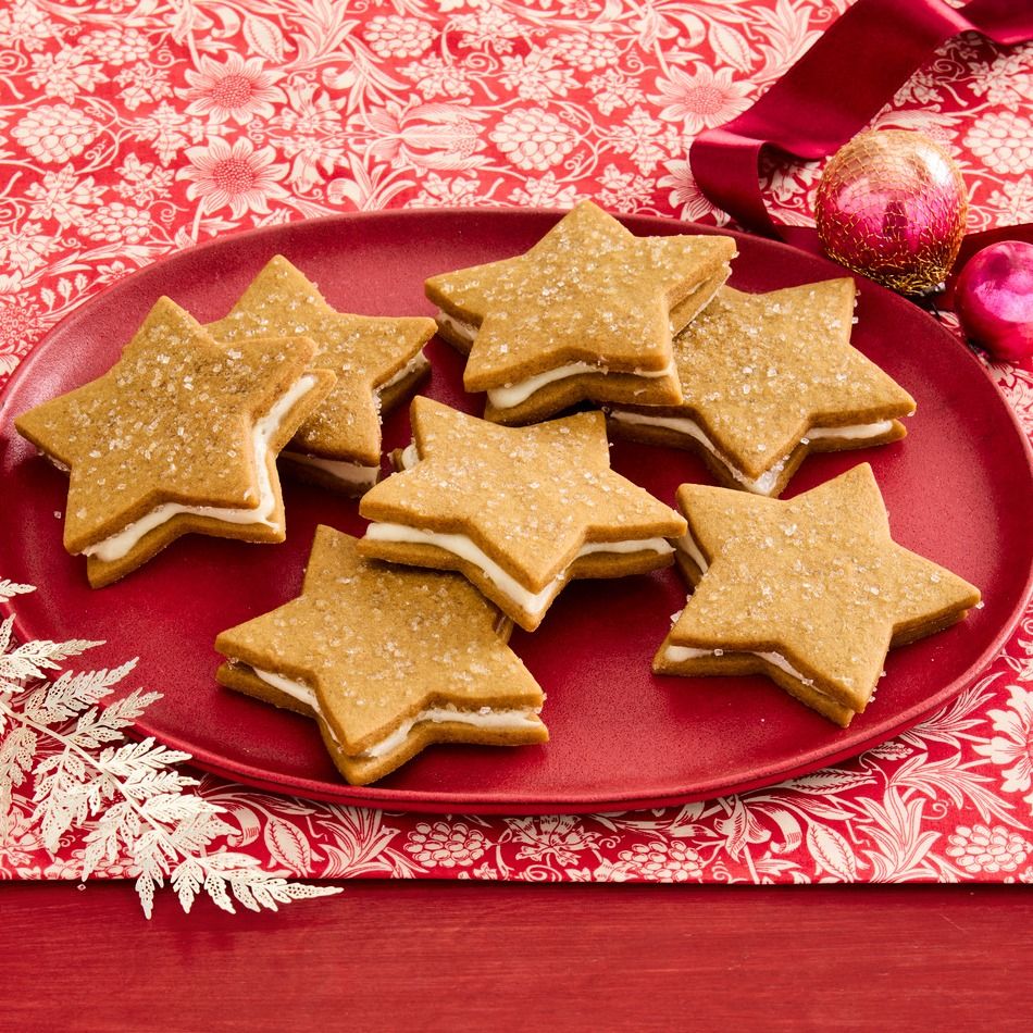 Star-shaped gingerbread sandwich cookies with white cream filling on red plate with Christmas ornaments