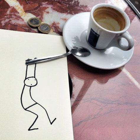 Stick figure drawing on paper seemingly holding a spoon beside an espresso coffee cup on a marble table