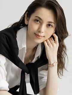 Woman with long brown hair in white blouse and black scarf posing with a soft smile