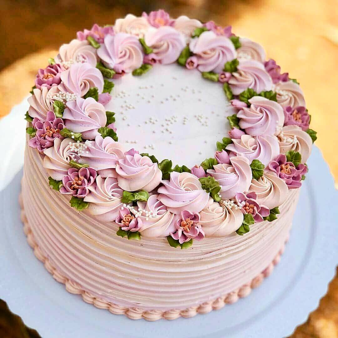 Pink frosted cake with buttercream roses and white flowers arranged in a circle on top