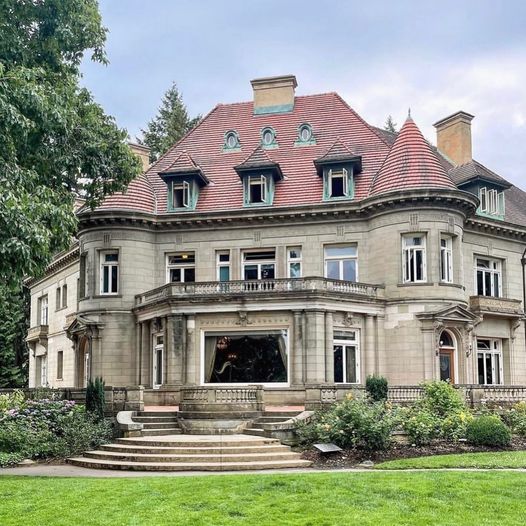Historic stone mansion with red tile roof and columned entrance on green lawn