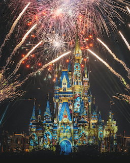Cinderella Castle lit up at night with colorful fireworks exploding above it