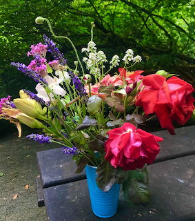 Mixed flower bouquet with roses and wildflowers in blue vase on outdoor stone table with garden background
