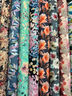 Vertical rolls of floral patterned fabrics in various colors including teal, orange, pink, and blue with flower and leaf designs