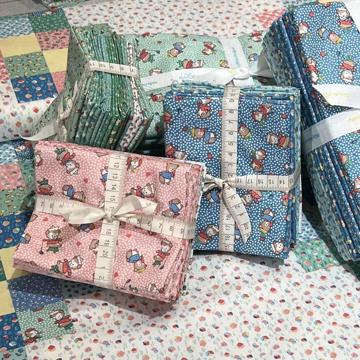 Tied bundles of patterned quilting fabric in pink, blue, and green floral prints arranged on dotted cloth