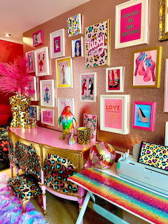 Bright pink gallery wall with multiple colorful frames above console table with rainbow striped bench