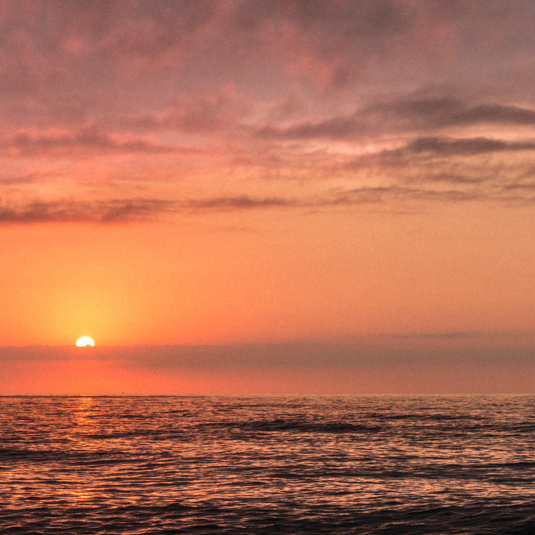 Orange sunset over a calm ocean with soft clouds and light reflecting on the water