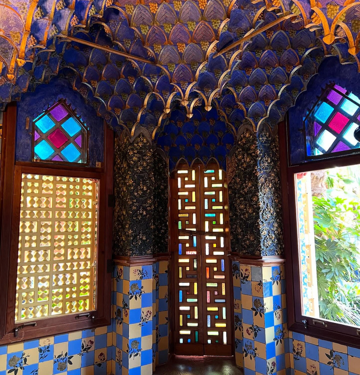 Ornate Moorish interior with blue tiles, geometric patterns, carved ceiling, and colorful stained glass windows