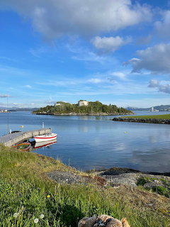 Small boats on calm coastal water beside a grassy shore under a blue sky in Stavanger, Norway.
