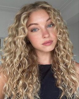 Portrait of woman with long blonde curly hair and blue eyes wearing black top
