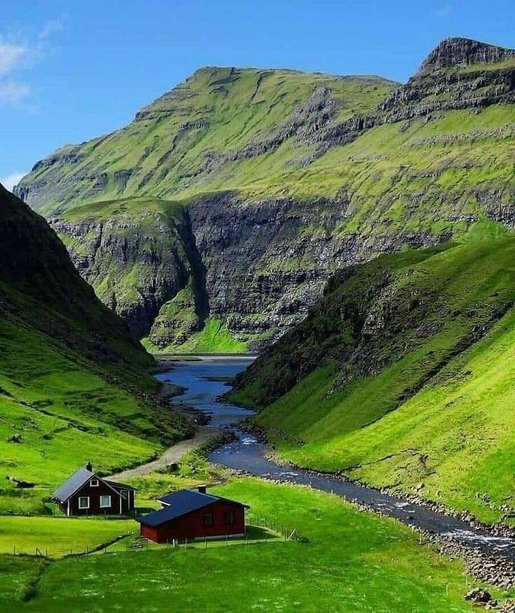 Steep green mountain valley in Faroe Islands with stream and small black house