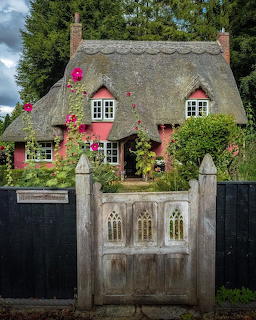 Thatched roof cottage with pink climbing roses and decorative wooden gate entrance