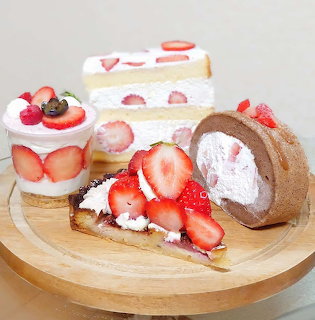 Wooden platter with strawberry cakes, rolled cake, waffle topped with whipped cream and fresh strawberries