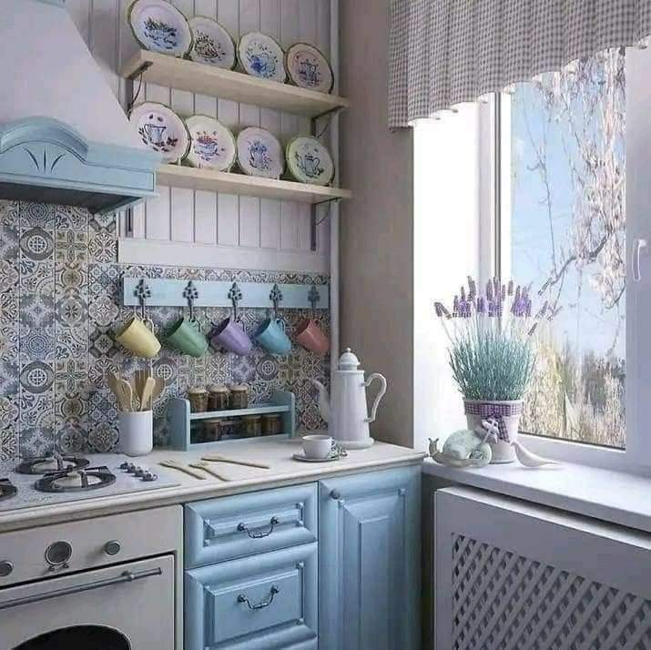 Light blue cottage kitchen with patterned tiles, hanging mugs, plate shelf, stove, and window with lavender