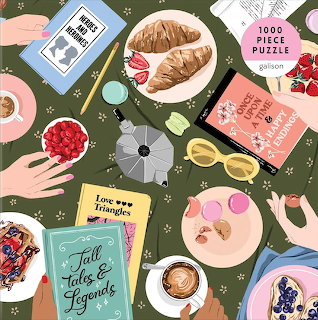 Flat lay of books, croissants, berries, coffee cups, and hands on a green table with floral pattern