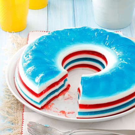 Ring-shaped red, white, and blue layered gelatin mold with a slice removed, on a white plate