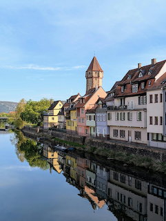 Colorful riverside houses and a tower reflected in calm water under blue sky