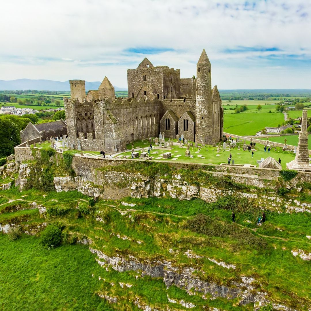 Aerial view of Rock of Cashel medieval castle ruins on hilltop with green fields and cemetery