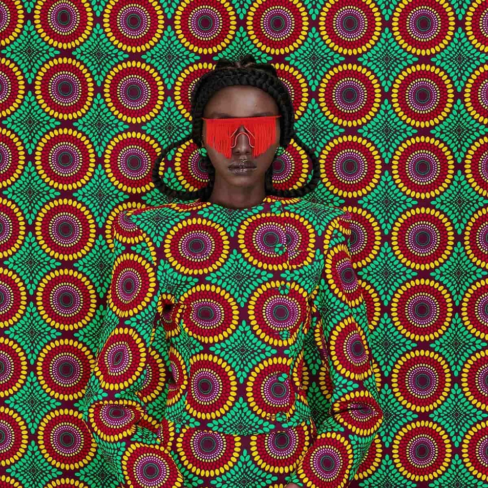 Woman in a colorful patterned outfit with red visor glasses against a matching patterned backdrop