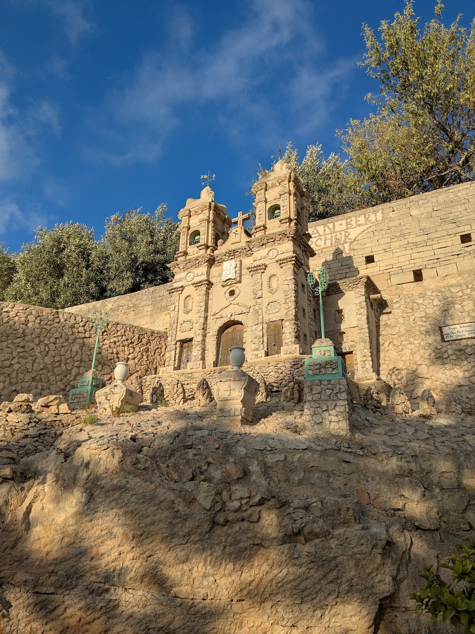 Stone baroque church facade with bell towers built into a limestone wall, viewed from below, Malta