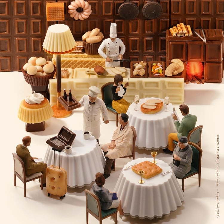 Miniature figures seated at tables in a restaurant constructed from chocolate bars, wafers, and various desserts